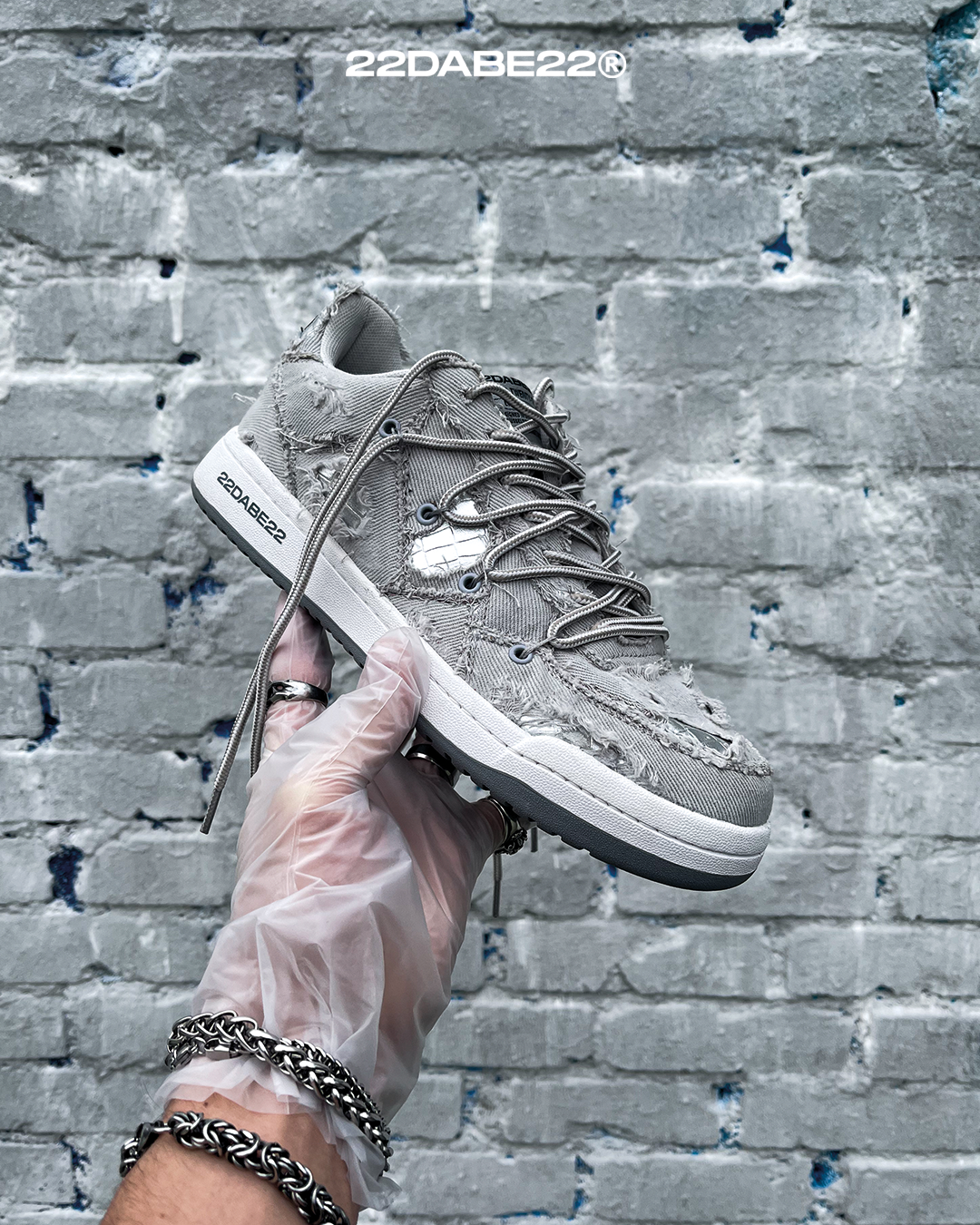 The DABE RANGER TWENTYTWO GREY shoe, a streetwear statement piece with metallic details under denim fabric on the upper. The shoe features double laces for extra style and versatility. Each shoe is handmade and unique, with every hole made by hand, giving it a one-of-a-kind look. The shoe is perfect for those who want to stand out from the crowd and make a fashion statement.