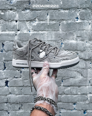 The DABE RANGER TWENTYTWO GREY shoe, a streetwear statement piece with metallic details under denim fabric on the upper. The shoe features double laces for extra style and versatility. Each shoe is handmade and unique, with every hole made by hand, giving it a one-of-a-kind look. The shoe is perfect for those who want to stand out from the crowd and make a fashion statement.