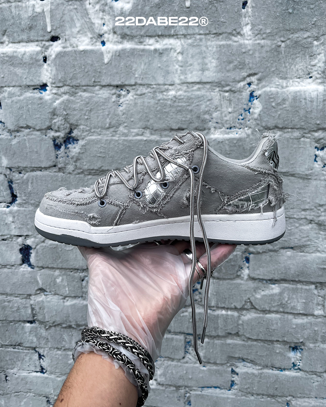 The DABE RANGER TWENTYTWO GREY shoe, a streetwear statement piece with metallic details under denim fabric on the upper. The shoe features double laces for extra style and versatility. Each shoe is handmade and unique, with every hole made by hand, giving it a one-of-a-kind look. The shoe is perfect for those who want to stand out from the crowd and make a fashion statement.